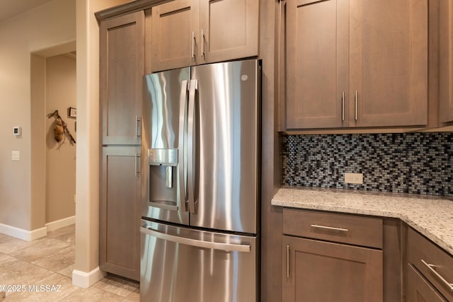 kitchen featuring light stone counters, stainless steel fridge with ice dispenser, decorative backsplash, and light tile patterned floors