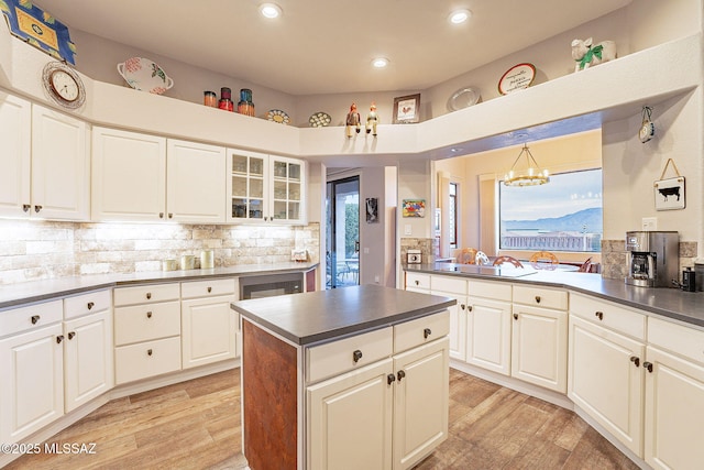 kitchen with white cabinetry, light hardwood / wood-style flooring, a notable chandelier, pendant lighting, and backsplash