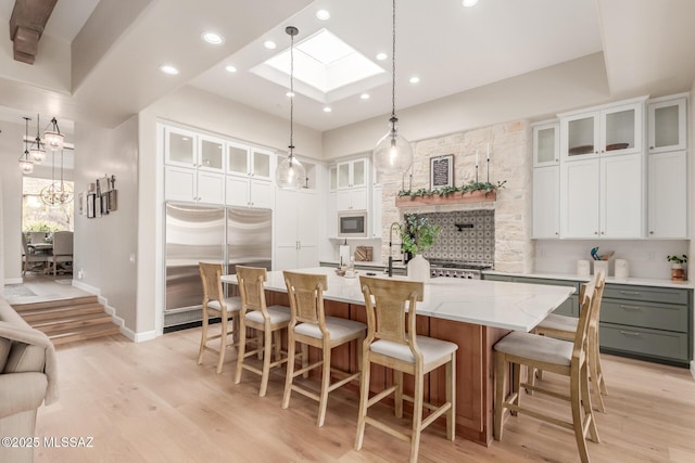 kitchen with built in appliances, white cabinetry, hanging light fixtures, and a kitchen island with sink