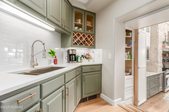 kitchen with decorative backsplash, sink, green cabinetry, and light hardwood / wood-style floors