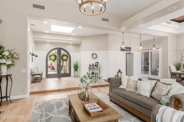 living room with light hardwood / wood-style flooring, a notable chandelier, a skylight, and french doors