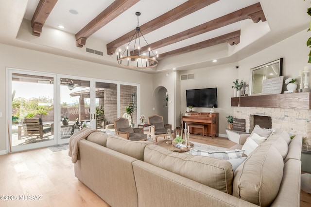 living room featuring a fireplace, beam ceiling, a chandelier, and light wood-type flooring