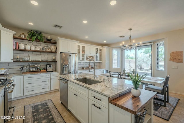 kitchen featuring a center island with sink, a sink, stainless steel appliances, and open shelves