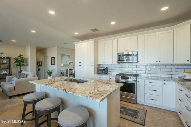 kitchen with a sink, tasteful backsplash, light stone countertops, stainless steel appliances, and visible vents