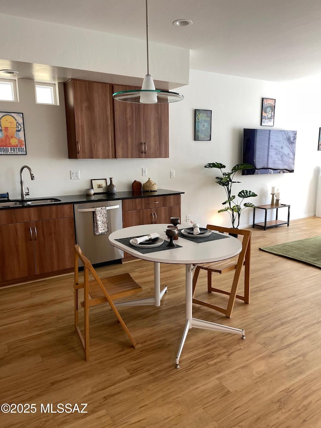 kitchen featuring hanging light fixtures, dishwasher, sink, and light hardwood / wood-style flooring