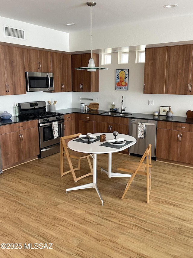 kitchen featuring pendant lighting, stainless steel appliances, sink, and light wood-type flooring