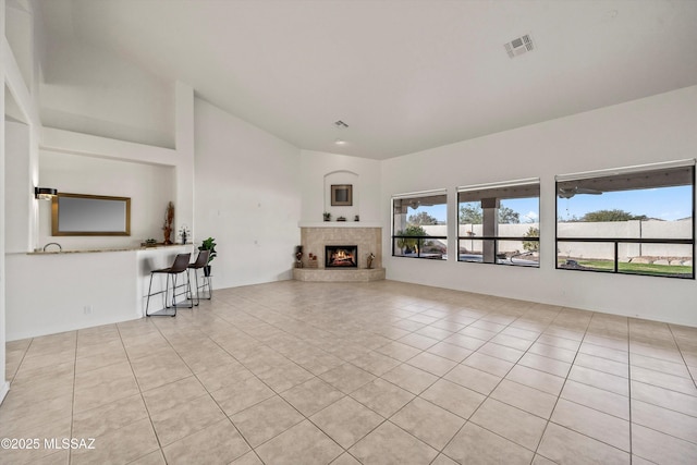 unfurnished living room with a tiled fireplace, light tile patterned floors, and lofted ceiling