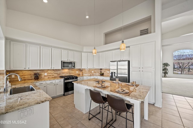 kitchen featuring sink, stainless steel appliances, a high ceiling, light stone countertops, and decorative light fixtures