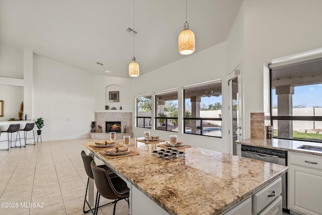 kitchen with a fireplace, decorative light fixtures, white cabinetry, light tile patterned floors, and light stone countertops