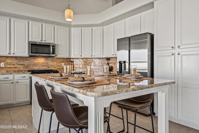 kitchen with a kitchen island, decorative light fixtures, white cabinets, light stone counters, and stainless steel appliances