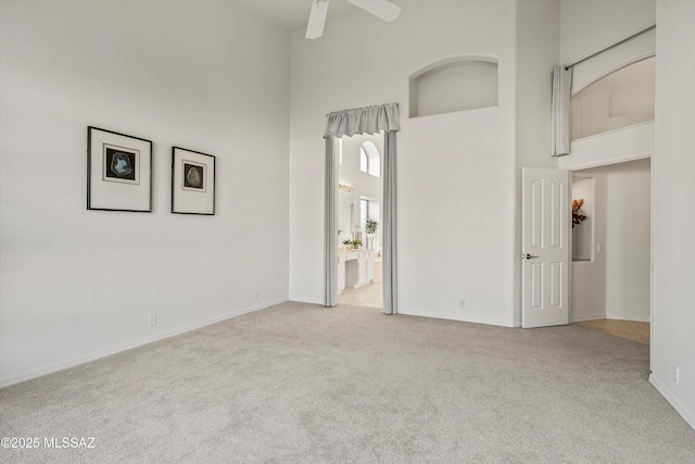 spare room with ceiling fan, light carpet, and a high ceiling