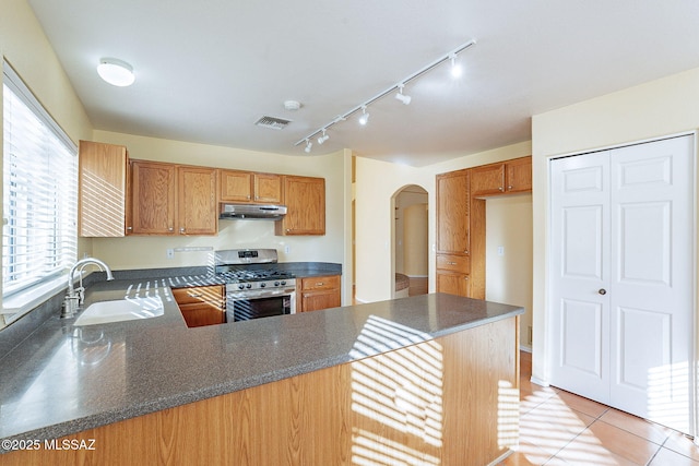 kitchen featuring light tile patterned flooring, sink, stainless steel range with gas stovetop, and kitchen peninsula