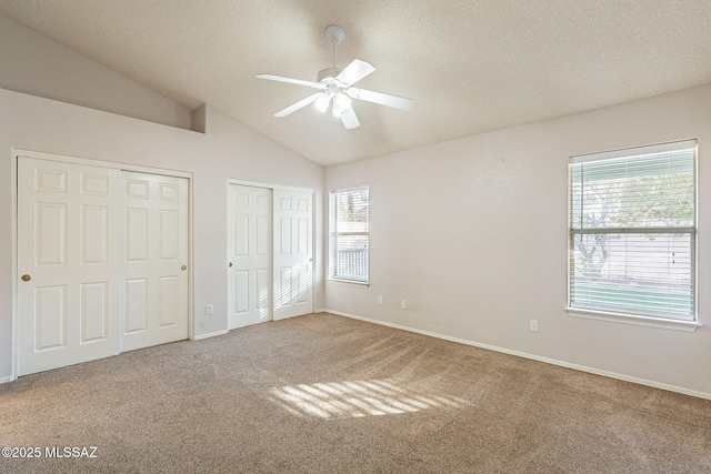 unfurnished bedroom with vaulted ceiling, carpet floors, ceiling fan, multiple closets, and a textured ceiling