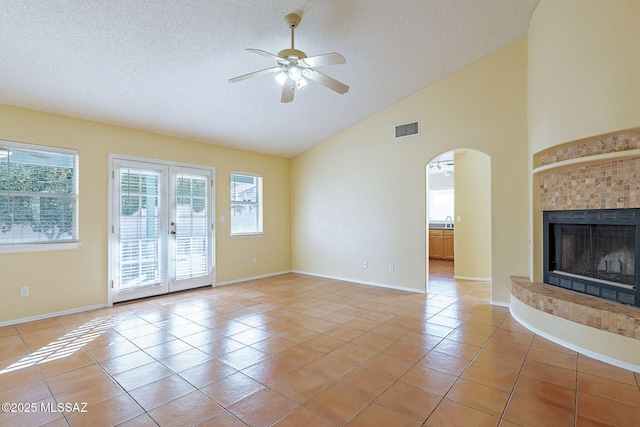 unfurnished living room featuring lofted ceiling, a tile fireplace, a textured ceiling, light tile patterned flooring, and french doors