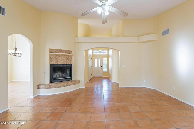 unfurnished living room featuring a high ceiling, ceiling fan with notable chandelier, light tile patterned floors, and a fireplace