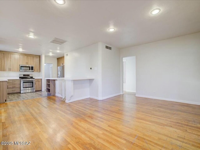 kitchen with light wood-type flooring, stainless steel appliances, a kitchen bar, and kitchen peninsula