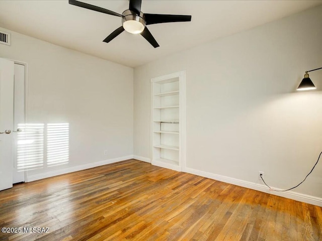 spare room with built in shelves, ceiling fan, and hardwood / wood-style flooring