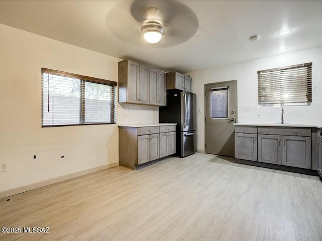 kitchen featuring light hardwood / wood-style floors, tasteful backsplash, stainless steel fridge, and ceiling fan