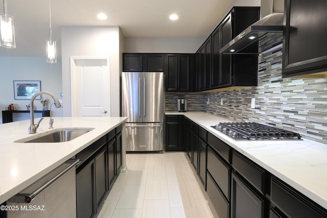 kitchen with appliances with stainless steel finishes, sink, hanging light fixtures, light stone countertops, and wall chimney range hood