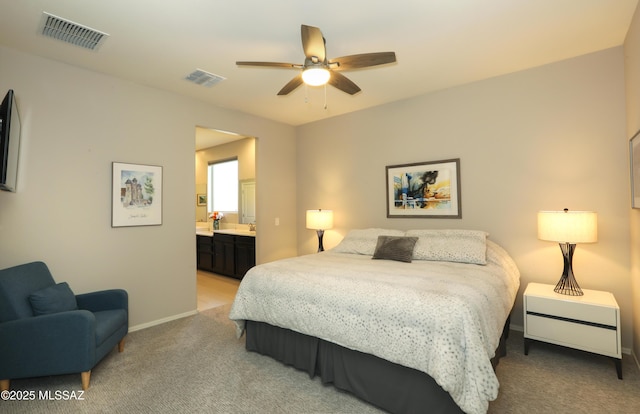 bedroom with ceiling fan, light colored carpet, and connected bathroom