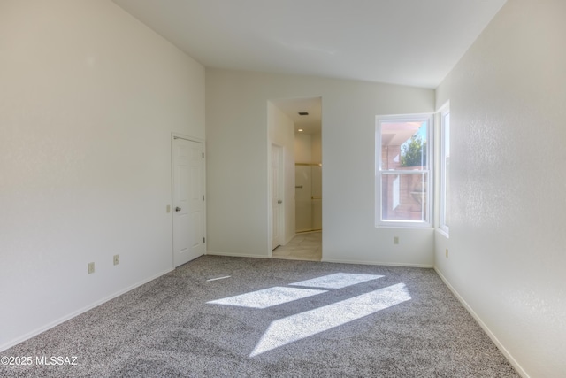 unfurnished bedroom with vaulted ceiling, ensuite bathroom, and light colored carpet