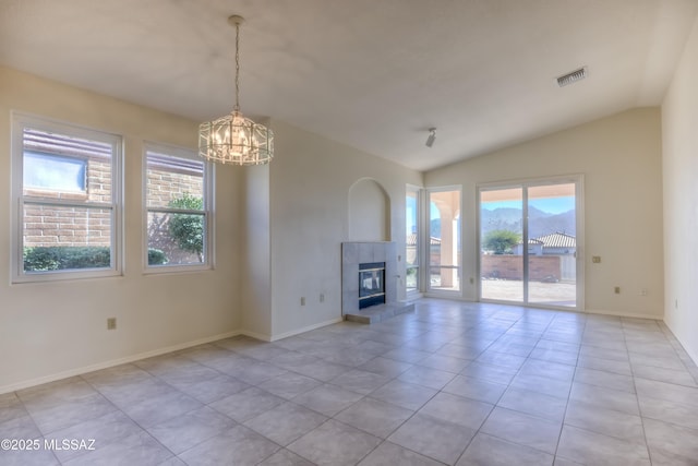 unfurnished living room with light tile patterned floors, a tile fireplace, vaulted ceiling, and a notable chandelier