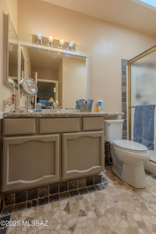 bathroom featuring toilet, a stall shower, stone finish floor, and vanity