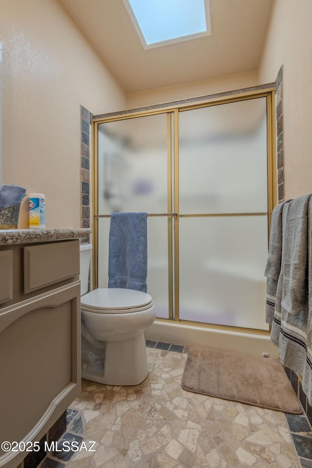full bath featuring toilet, a skylight, vanity, a shower stall, and stone finish floor