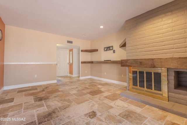 unfurnished living room featuring baseboards, visible vents, stone finish flooring, a fireplace, and recessed lighting