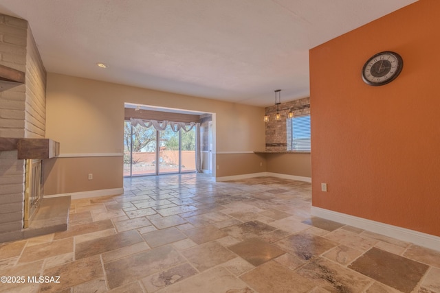 unfurnished living room featuring a brick fireplace, stone tile flooring, and baseboards