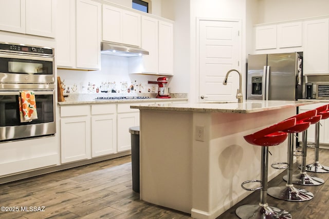 kitchen featuring white cabinetry, stainless steel appliances, light stone countertops, and an island with sink