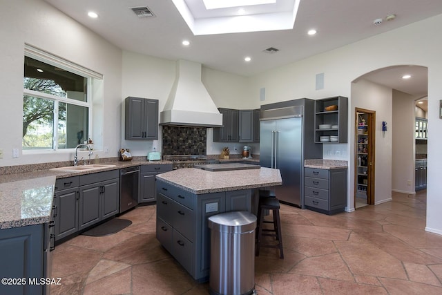 kitchen with premium range hood, sink, a skylight, appliances with stainless steel finishes, and a kitchen island