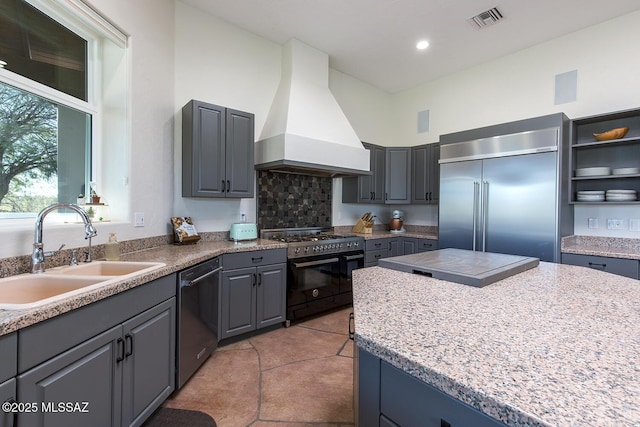 kitchen featuring sink, high end appliances, gray cabinets, custom range hood, and light stone countertops