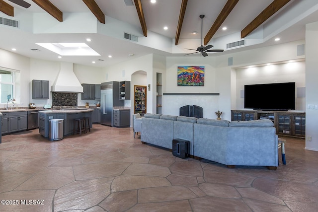 living room featuring sink, a towering ceiling, beamed ceiling, and ceiling fan