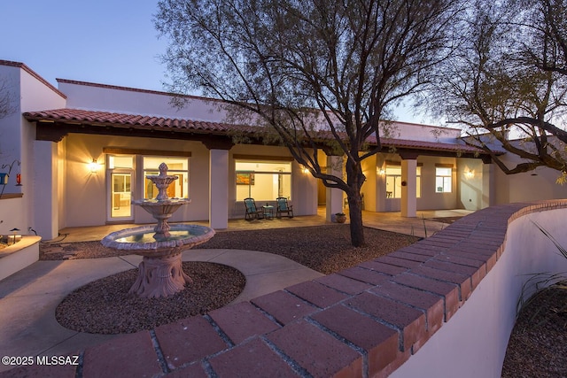 back house at dusk featuring a patio area