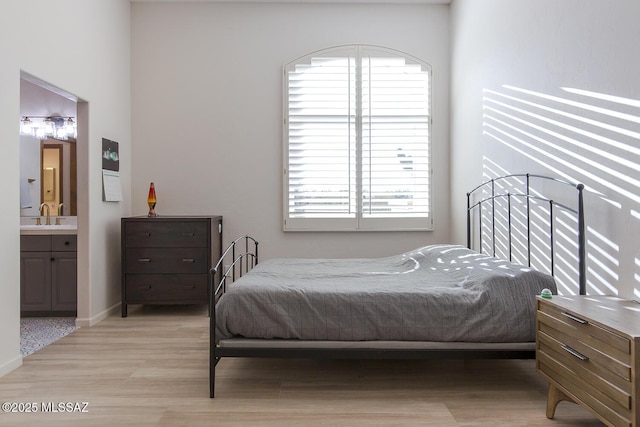 bedroom with connected bathroom, light hardwood / wood-style floors, and sink