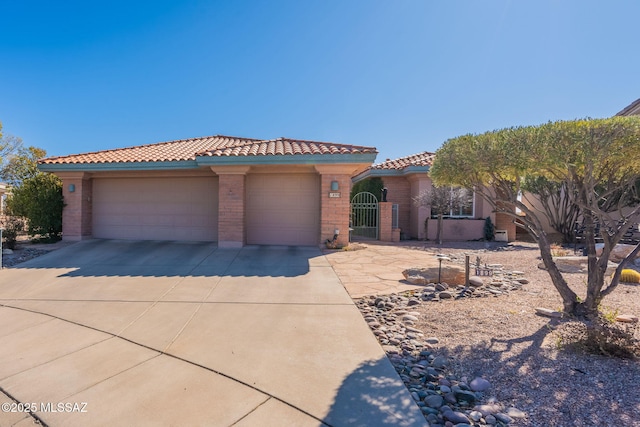 mediterranean / spanish house with an attached garage, brick siding, concrete driveway, a tiled roof, and a gate