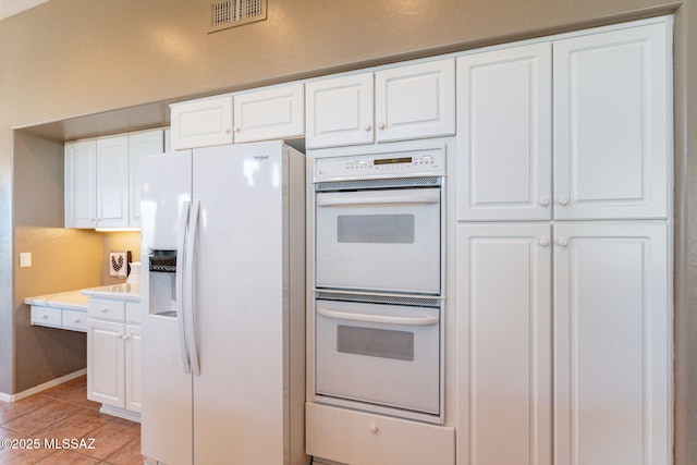 kitchen with light tile patterned flooring, white appliances, visible vents, white cabinetry, and light countertops