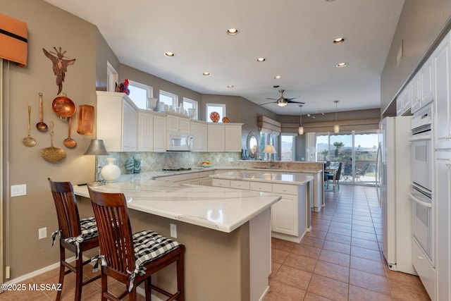 kitchen with tasteful backsplash, white appliances, white cabinetry, and a peninsula