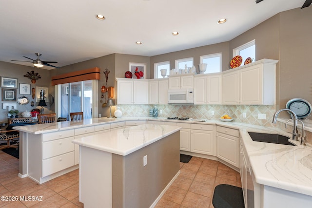 kitchen featuring a peninsula, white microwave, plenty of natural light, and a sink