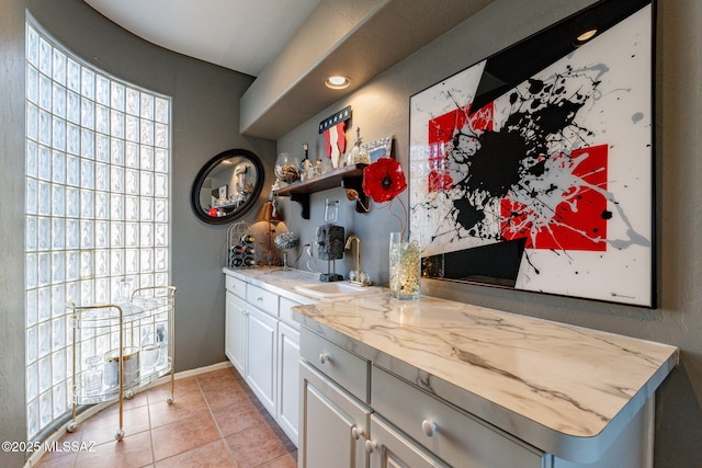 interior space featuring light tile patterned floors, baseboards, indoor wet bar, and a sink