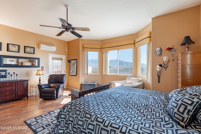 bedroom with ceiling fan, a mountain view, a wall mounted AC, and wood finished floors