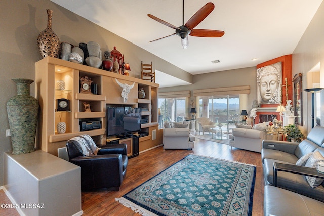 living area featuring a ceiling fan, a glass covered fireplace, visible vents, and wood finished floors