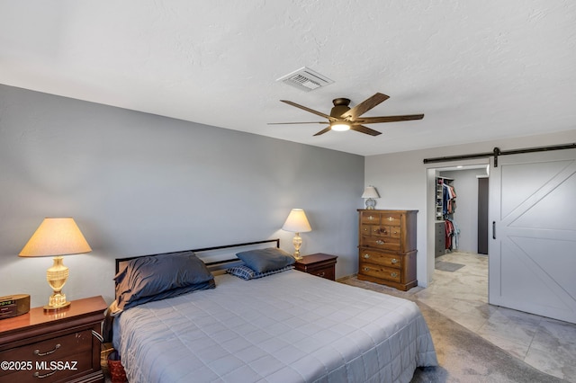 bedroom featuring ceiling fan, a barn door, and a walk in closet