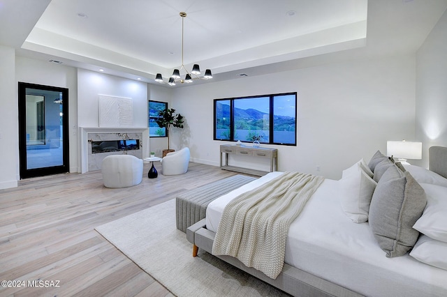 bedroom featuring an inviting chandelier, light hardwood / wood-style flooring, a raised ceiling, and a fireplace