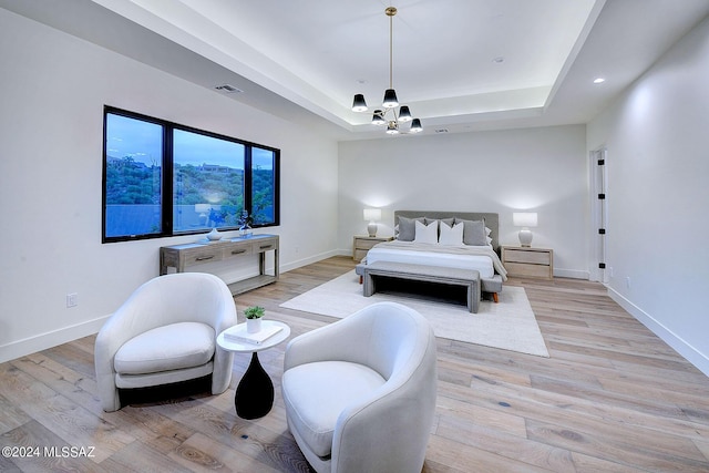 bedroom featuring an inviting chandelier, light hardwood / wood-style flooring, and a raised ceiling