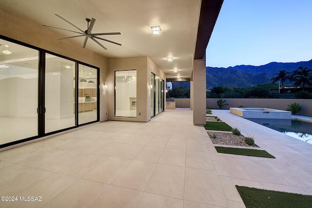 patio terrace at dusk featuring a pool with hot tub, a mountain view, and ceiling fan