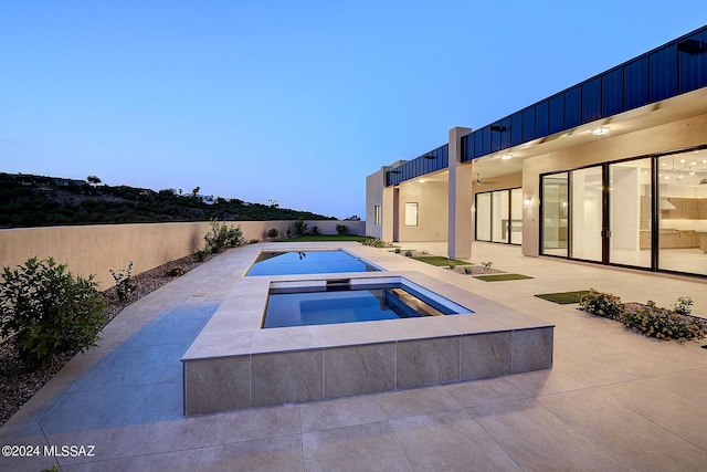 pool at dusk with an in ground hot tub and a patio