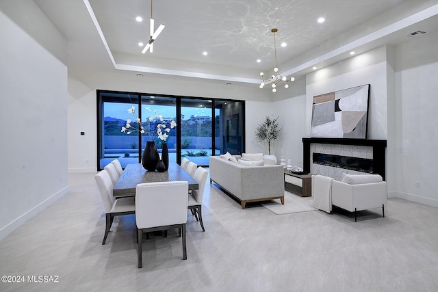 dining area with a raised ceiling, a notable chandelier, and a fireplace