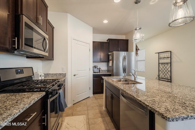 kitchen featuring pendant lighting, sink, appliances with stainless steel finishes, light stone counters, and an island with sink